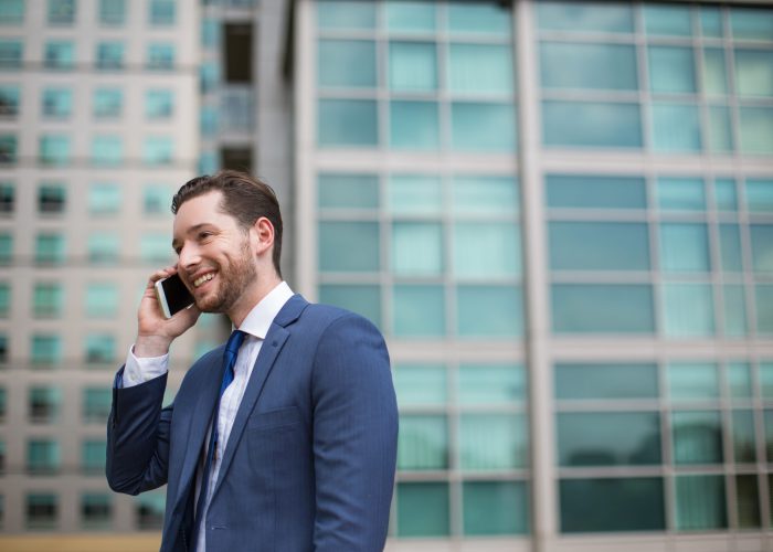 Closeup portrait of smiling middle-aged business man talking on mobile phone and standing with blurred office building in background